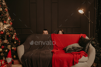 man and a woman hid behind couch. heads of a man and a woman stick out from behind sofa