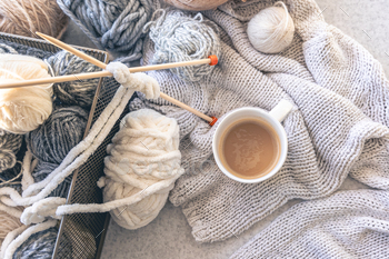 Yarn threads, knitted elements and a cup of coffee, top view.