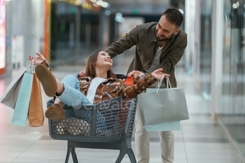 Riding in a shopping cart. Young couple are in supermarket together