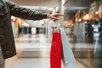 Red and blue colored shopping bags in hands, close up view. Man is shopping in the supermarket