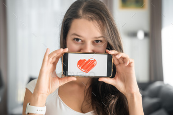 World Health Day concept. Young woman showing illustration of heart on her smartphone, illustrating