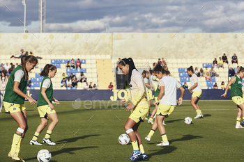 Female soccer players in green and yellow uniforms practicing on the field with a ball