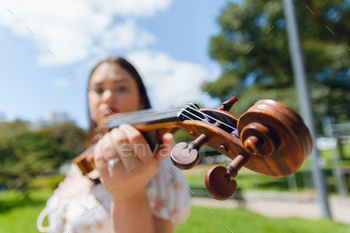 wide angle portrait of blurred unrecognizable woman holding her violin in street, focus on violin