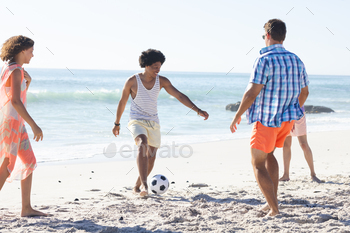Diverse friends play soccer on the beach, enjoying the sun and sand