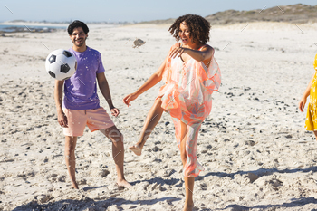 Young biracial couple enjoys a soccer game on the beach