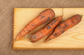Three raw carrots at wooden board on canvas