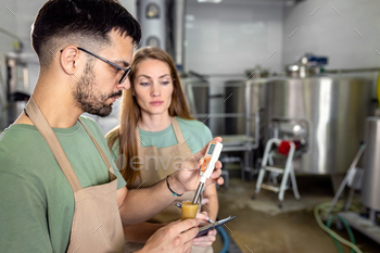Man and woman working in craft brewery checking the pH value of the beer.