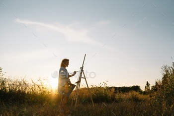 Silhouette of a blonde girl artist. Lady paints a painting on the canvas with the help of paints