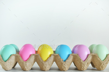 Colorful pastel Easter eggs in a carton on plain white background