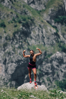 A sportswoman is achieving a goal and standing on a cliff in mountains.