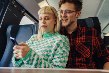 A hipster couple is buying online train ticket on phone app in train.