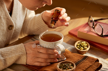 Woman add essential oil to her herbal infusion drink