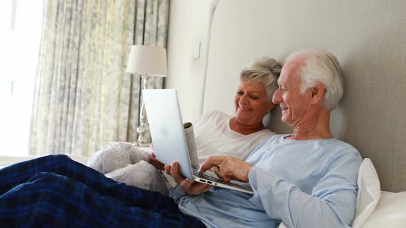 Smiling senior couple using laptop on bed in bedroom