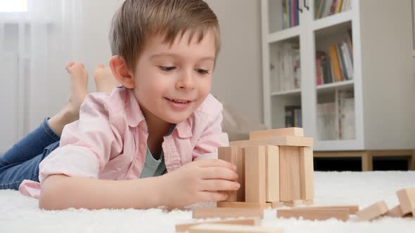 Smiling Boy Lying on Floor and Building House or Tower From Wooden Blocks