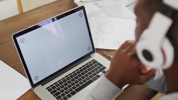 African american male teenager wearing headphones having video call using laptop with copy space