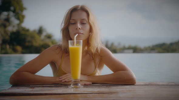 A Blonde Woman Drinks Mango Shake While Lounging in the Sun By the Pool on Vacation