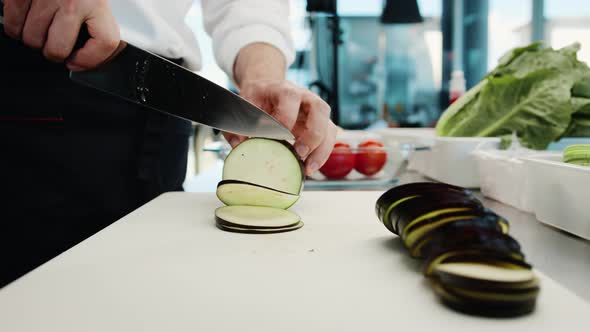 Close-up: A chef cuts an eggplant with fine pressure on a cutting surface in a professional kitchen