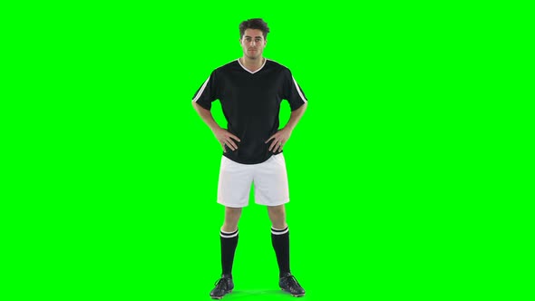 Confident football player standing against green screen