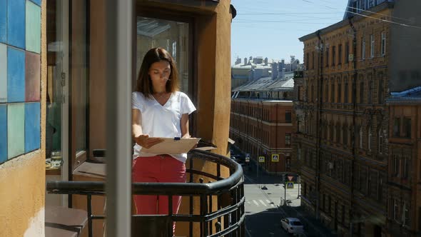 Dark-Haired Girl Painting Outside On Balcony In The Downtown.