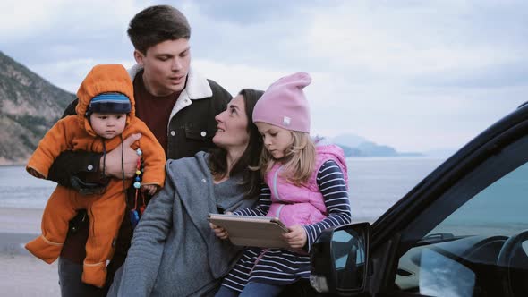 Family with children looking at a map on a tablet next to a car in nature.