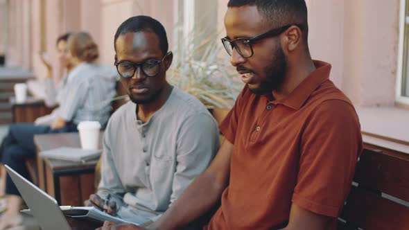 Afro-American Male Colleagues Using Laptop in Outdoor Coffee Shop