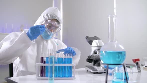 Scientist in PPE suite doing some research checking a liquid in a test tube at laboratory.