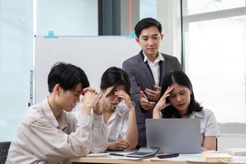 A team of Asian businessmen discusses managing stressful office work in an office conference room.