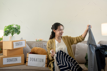 Woman asian holding donation box full with clothes and select clothes. Concept of donation and