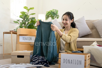 Woman asian holding donation box full with clothes and select clothes. Concept of donation and