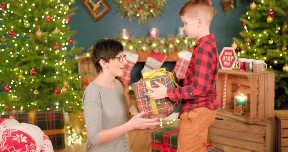 Son is giving a present to his mum while she is smiling out of happiness