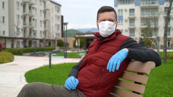 Man in a Face Mask Sits on a Bench