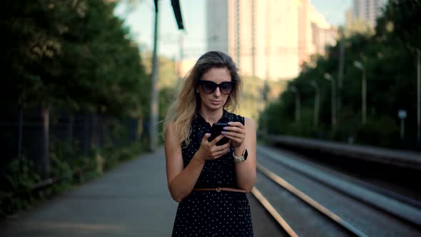 Woman Using Mobile Phone And Waiting Public Transport On Train Station. Active Lifestyle On Vacation
