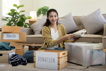 Woman asian holding donation box full with clothes and select clothes. Concept of donation and