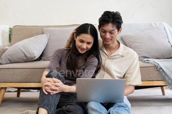 Happy asian couple using laptop sit relax on floor doing ecommerce shopping online on website at