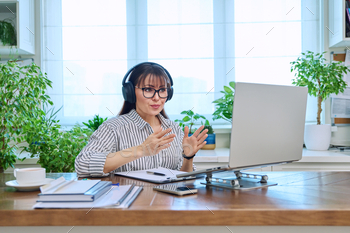Mature woman in headphones having video conference using computer in home office