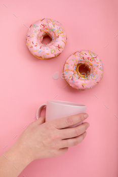 Sweet donuts on a pink background female hand holds a pink mug with coffee. Game of color, color