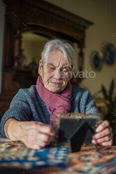 Elderly woman concentrating on a puzzle at home.