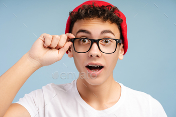 Shocked smart school boy with braces wearing red hat and glasses looking at camera isolated