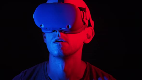 Man in a Virtual Reality Helmet Illuminated in Red and Blue Plays a Game