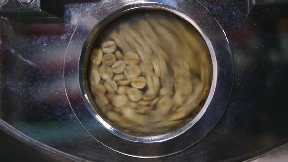 Close up of  freshly dried green coffee beans tumbling around in roasting machine