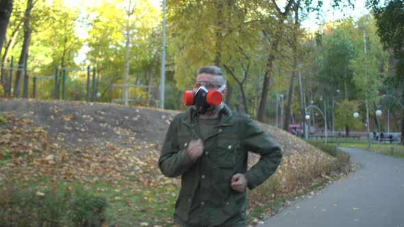 Middleaged Gray Beard Man in Respirator and Khaki Clothes Jogging in Park at Early Autumn