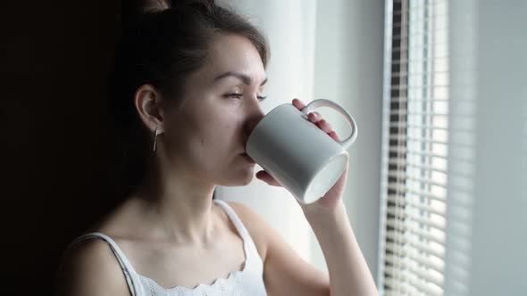 the girl goes to the window with a cup of coffee and pours red wine into it