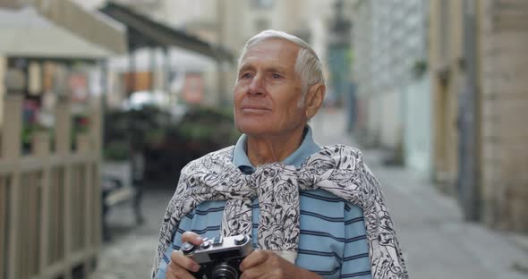 Senior Male Tourist Exploring Town and Makes a Photo with Retro Photo Camera