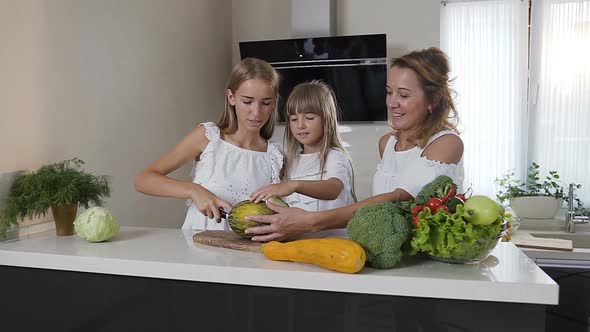 Two Sisters with Their Mother in White Dresses is Cooking Healthy Vegetable Salad