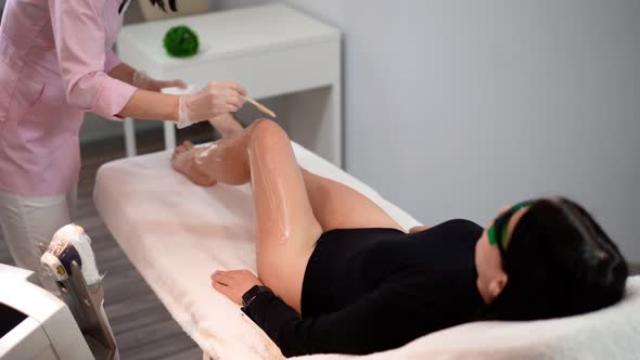 Beautician Doing Laser Hair Removal on Slim Legs Woman in Beauty Salon. 