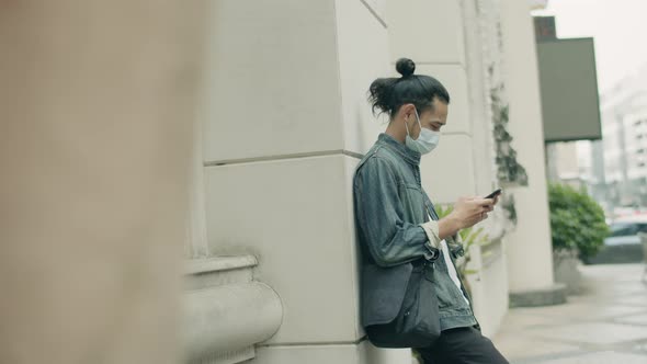 Young Asian man wearing a surgical mask and using smartphone.