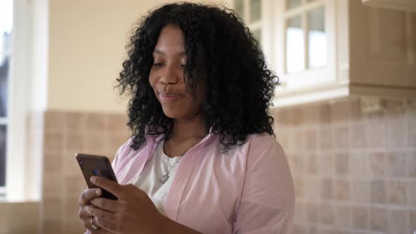 Portrait of Happy African American Woman Smiling Reading Message on Smartphone Standing in Kitchen