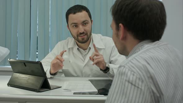 Male Bearded Doctor in Clinic Advertises Preparation To Client