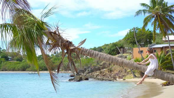 Adorable Little Girl Sitting on Palm Tree During Summer Vacation on White Beach