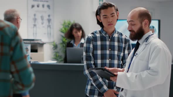 General Practitioner Talking to Asian Man About Diagnosis on Digital Tablet